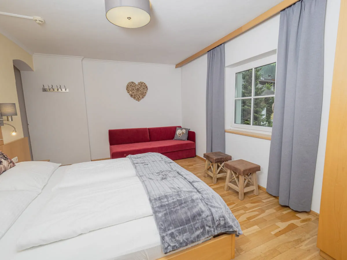 Schlafzimmer mit Bett, rotem Sofa und Fenster, Holzfußboden