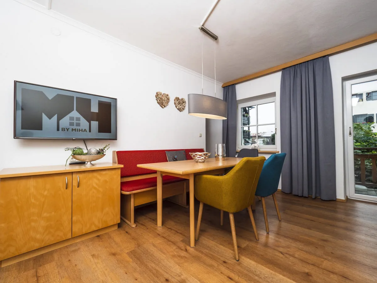 Wohnzimmer mit Tisch, bunten Stühlen und Fernseher an der Wand.