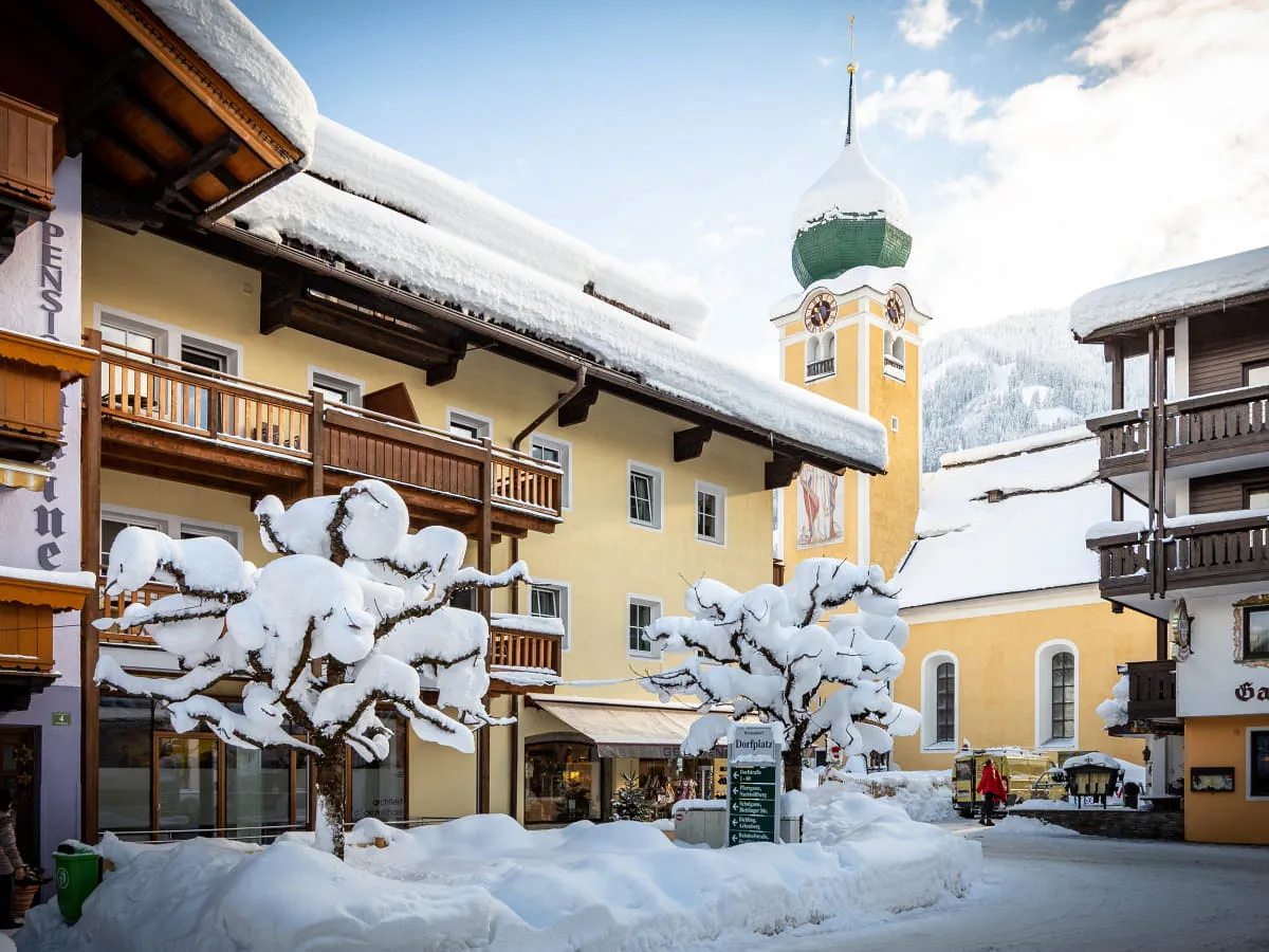 Winterliche Landschaft mit schneebedeckten Bäumen und einem Uhrturm in einem Dorf.