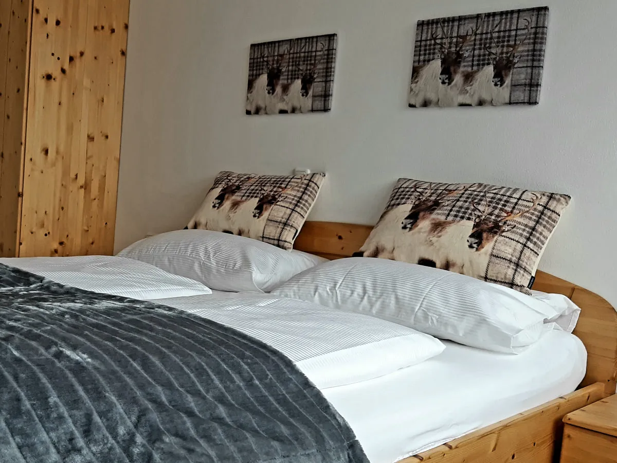 Schlafzimmer mit Holzmöbeln, Bett, grauer Decke und Bildern an der Wand