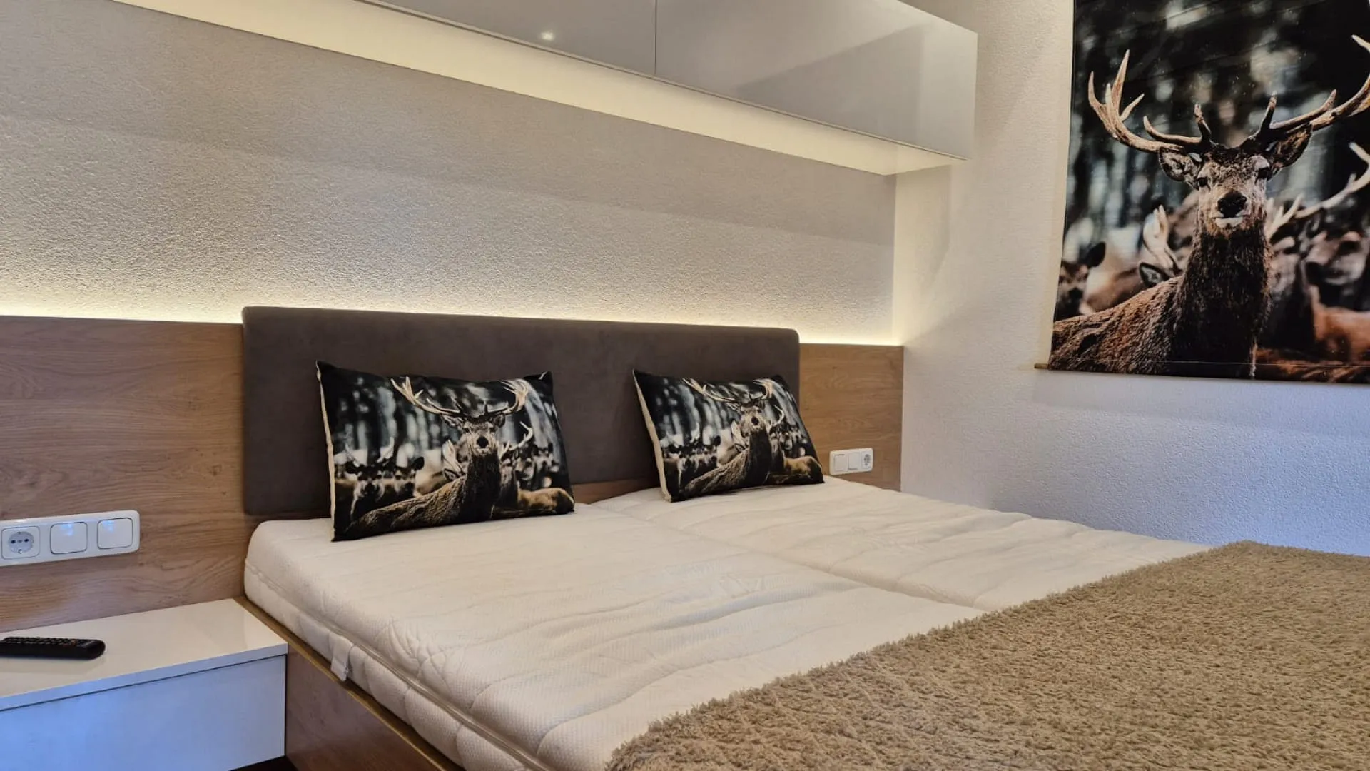 Schlafzimmer mit Bett, dekorativen Kissen und einem Bild eines Hirschs an der Wand